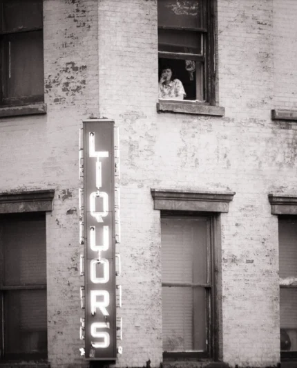 Personne à la fenêtre d'un immeuble avec enseigne de liquor store