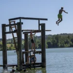 Enfants sauts d'une structure en bois dans un lac par une journée ensoleillée
