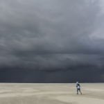 Promeneur solitaire sur une plage sous un ciel orageux