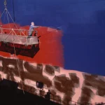 Peinture d'un navire par deux ouvriers sur une plateforme suspendue