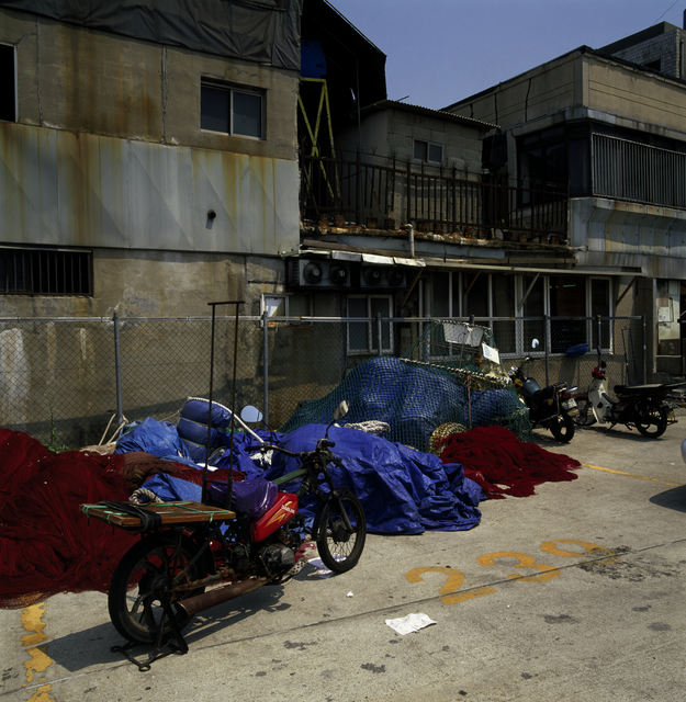 AKG964826.webp Cours de bâtiment dégradé avec des motos et filets de pêche – Image 1